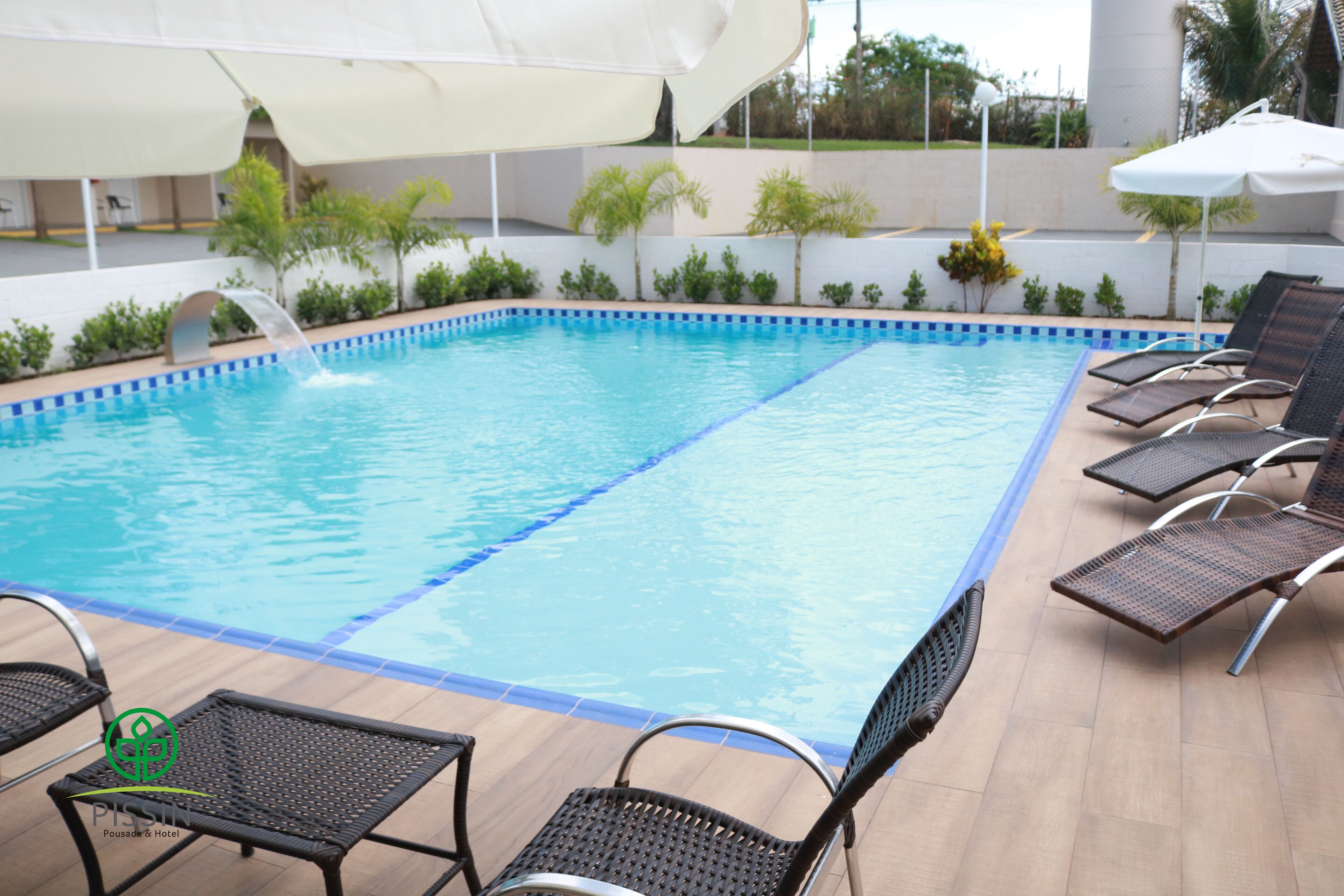 En swimmingpool med en fontän, omgiven av solstolar och parasoller.