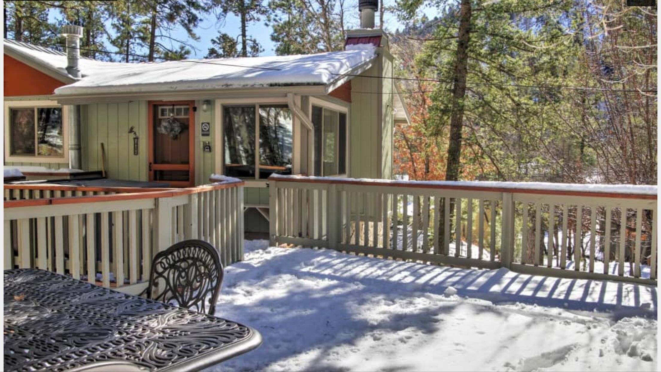 A covered deck with a railing, a table, and chairs in a snowy outdoor setting.