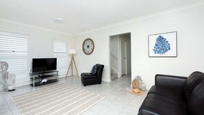 Un salon moderne doté d’un téléviseur à écran plat, d’un canapé en cuir noir, d’un fauteuil noir, d’un tapis à motifs et d’un escalier menant à un autre niveau.