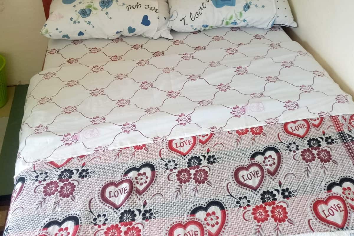 Ein Bett mit blumigem und herzförmigem Bettbezug, zwei Kissen mit dem Aufdruck 'I love you' und ein Holz-Kopfbrett.