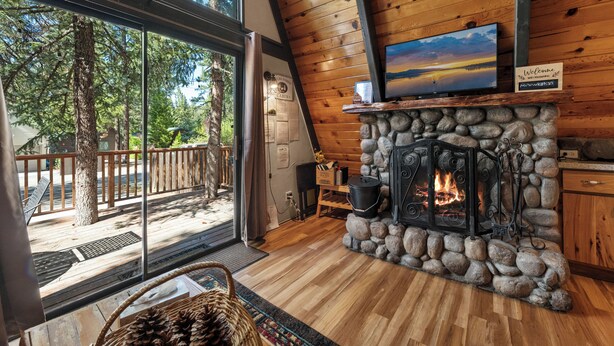 Ein Ferienhausinnenraum mit Kamin aus Stein, Holzwänden, einem großen Fenster und Blick ins Freie.