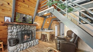 Ein Blockhaushaus-Interieur mit Kamin aus Stein, Holzboden, Ledersessel und einer Treppe.