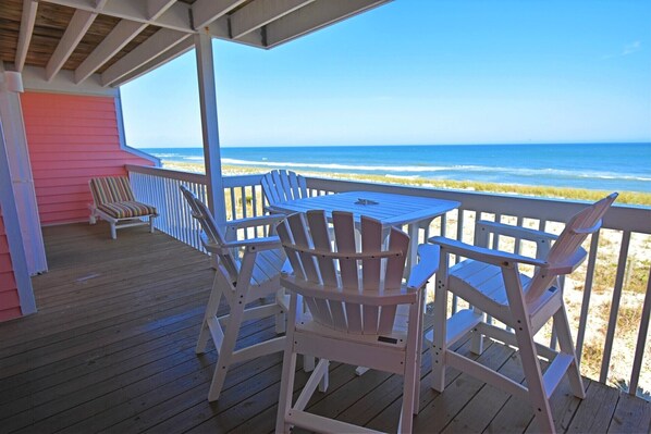 A wooden deck with Adirondack chairs and a table overlooking a beach.