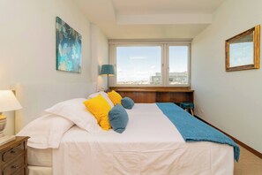 Une chambre à coucher bien rangée, avec un lit, une table de chevet, une lampe et une fenêtre donnant sur la ville.