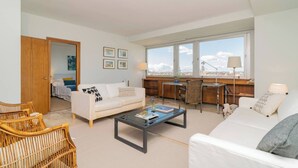 A modern living room with a sofa, coffee table, and a view of the city through large windows.