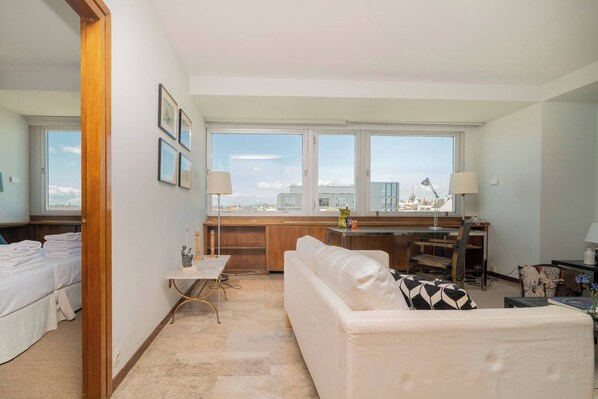 Una sala moderna con sofá, una mesita y vistas a la ciudad a través de amplios ventanales.