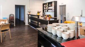 Uma cozinha moderna com piso de madeira escura, uma ilha central com pratos brancos empilhados e um armário preto com portas de vidro contendo utensílios de cozinha.