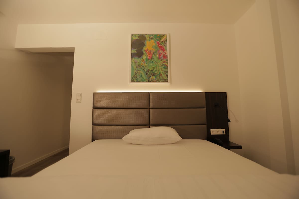 A hotel room with a large bed, a headboard with built-in lighting, a bedside table, and a wall-mounted artwork.