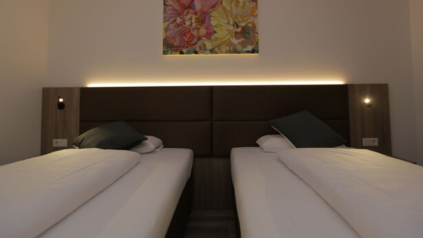 Quarto de hotel com duas camas, cabeceira com iluminação integrada e uma obra de arte floral na parede.