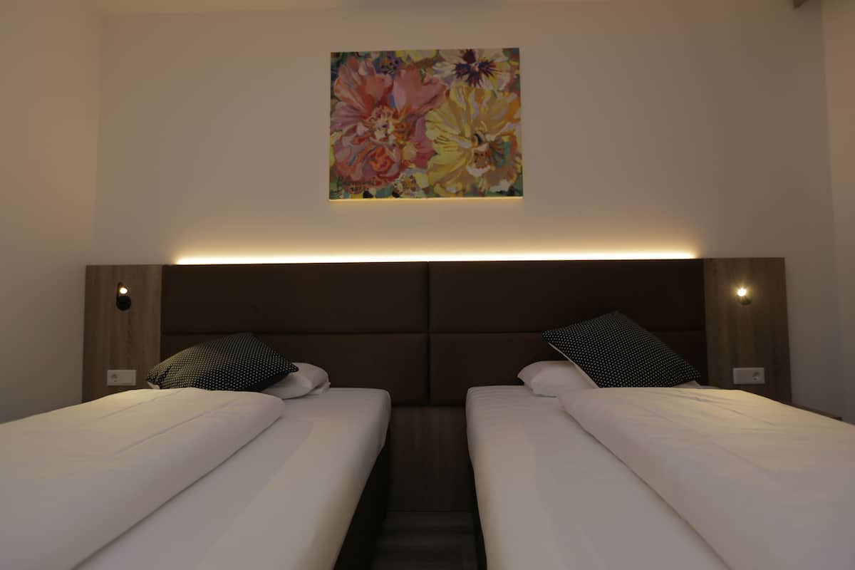 A hotel room with two beds, a headboard with integrated lighting, and a floral artwork on the wall.
