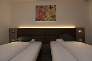 Een hotelkamer met twee bedden, een hoofdeinde met geïntegreerde verlichting en een bloemwerk op de muur.