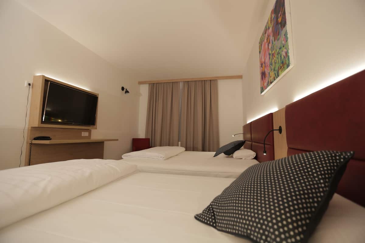 A hotel room with a bed, a TV, a desk, and a painting on the wall.