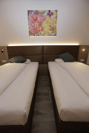 A hotel room with two single beds, a wooden headboard, and a colorful floral artwork on the wall. - Galeria Hotel Walldorf (Moerfelden-Walldorf)