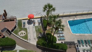 An aerial view of a resort with a swimming pool, sun loungers, palm trees, and a red umbrella. - Beach Front 2 bedroom 2 bath 7th floor condo in the prestigious Brigadune  (Myrtle Beach)