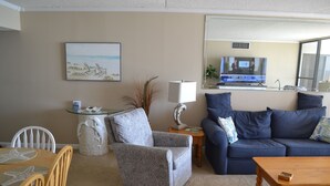 A living room with a blue sofa, a grey armchair, a wooden coffee table, a TV on a stand, and a painting on the wall. - Beach Front 2 bedroom 2 bath 7th floor condo in the prestigious Brigadune  (Myrtle Beach)