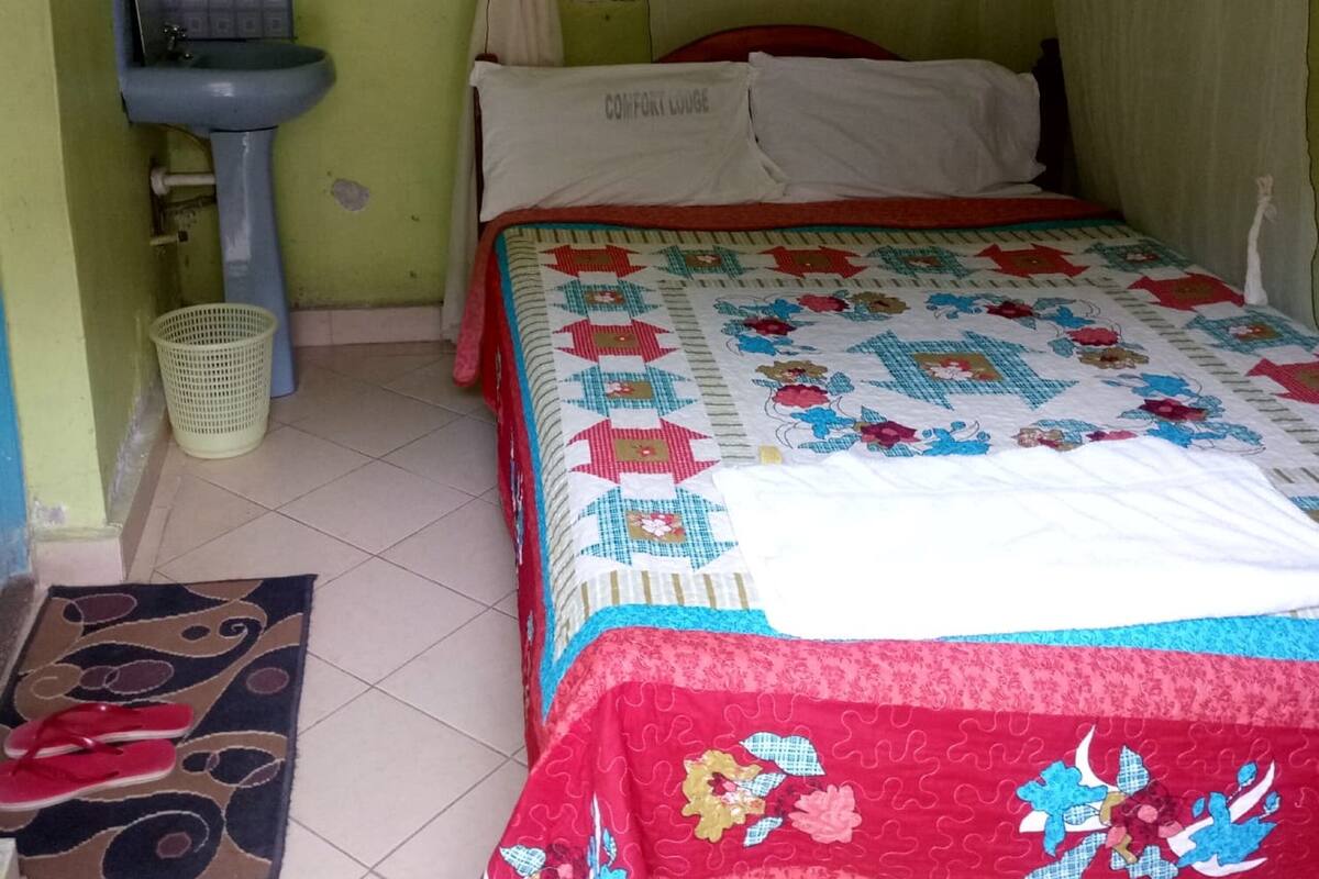 A bedroom with a bed, a bedside table, a sink, and a window with curtains.