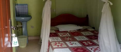 A bedroom with a bed covered by a canopy, a bedside table, a sink, and a mat on the floor.