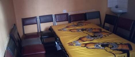 Un comedor con una mesa cubierta por un mantel amarillo con personajes de caricaturas, rodeado de sillas con asientos de cuero marrón y estructura de metal negro.