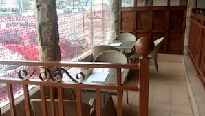 A dining area with wicker chairs and tables, large windows with a view of a parking lot, and a wooden interior. - Countryhouse Inn Hotel (Naivasha)