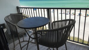 Un balcone con due sedie in vimini e un tavolino rotondo, con vista su una spiaggia con ombrelloni e persone.