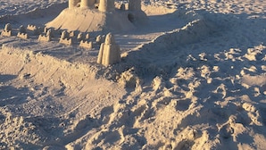 Una spiaggia sabbiosa con sculture in sabbia e un edificio moderno sullo sfondo.