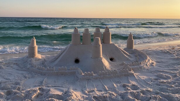 Un castello di sabbia su una spiaggia, con l'oceano sullo sfondo.