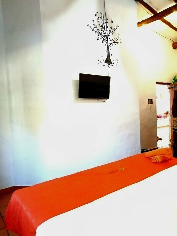 Une chambre avec un lit, un téléviseur fixé au mur et un motif décoratif représentant un arbre.