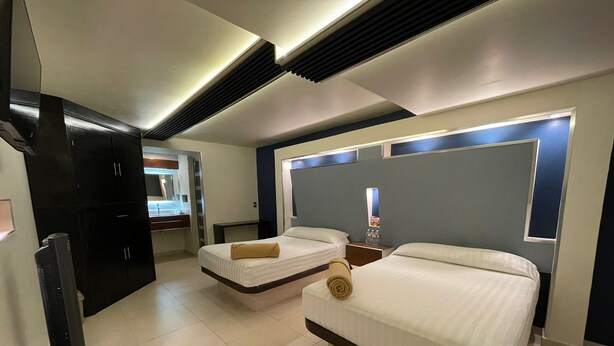 A hotel room with two beds, a flat-screen TV, and a bathroom with a mirror and sink. - Hotel Cuandón (Tepeji del Río de Ocampo)