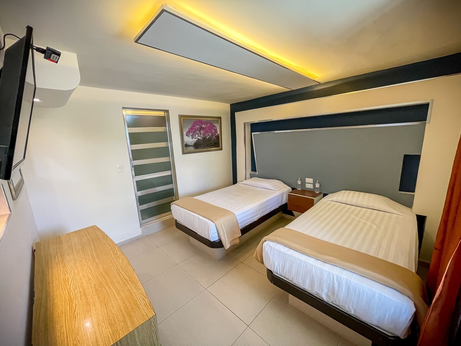 A hotel room with two beds, a desk, a TV, and a painting on the wall.