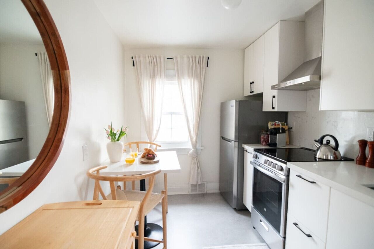 Une cuisine compacte comprenant une table à manger, des chaises, un réfrigérateur, un four et une bouilloire.