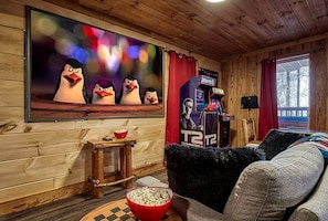 A cozy room with a wooden interior, a television mounted on the wall, a small table with a bowl of popcorn, and a couch.