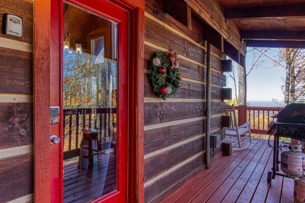A wooden cabin with a red door, a deck with outdoor seating, and a Christmas wreath.