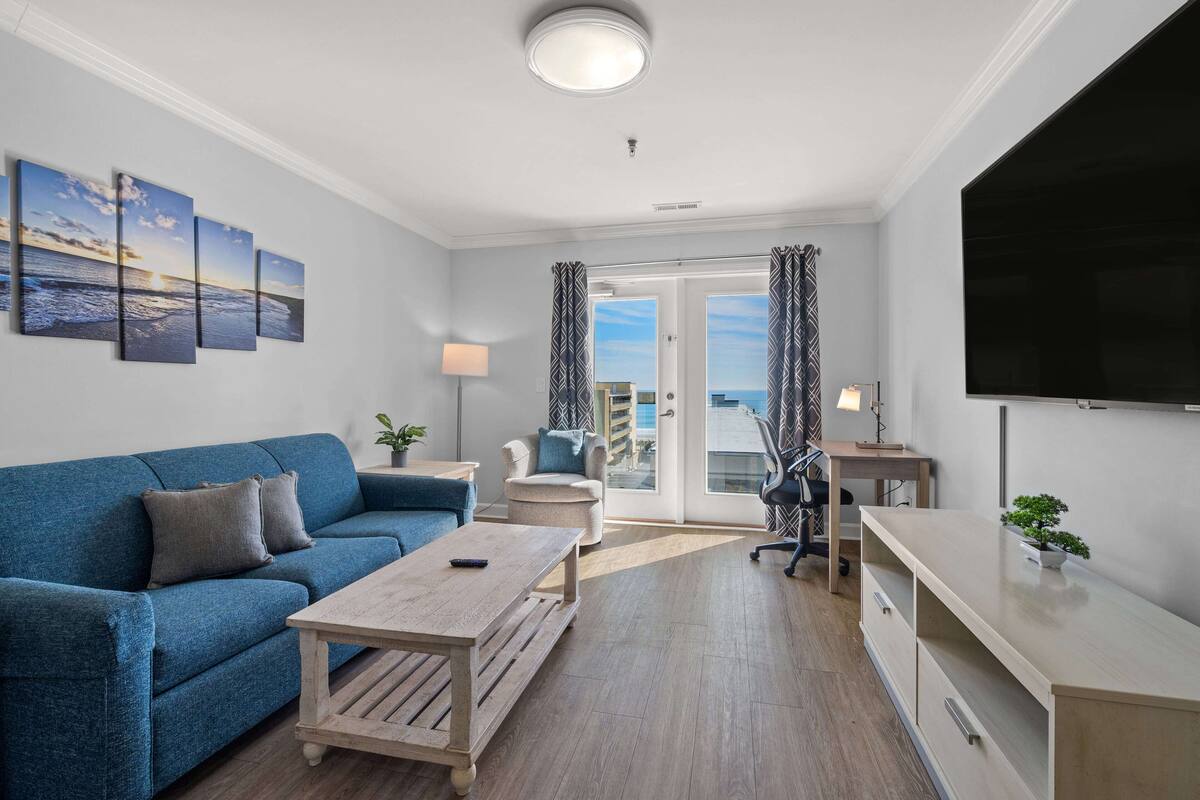 A modern living room with a blue sofa, a wooden coffee table, a desk, and a TV.