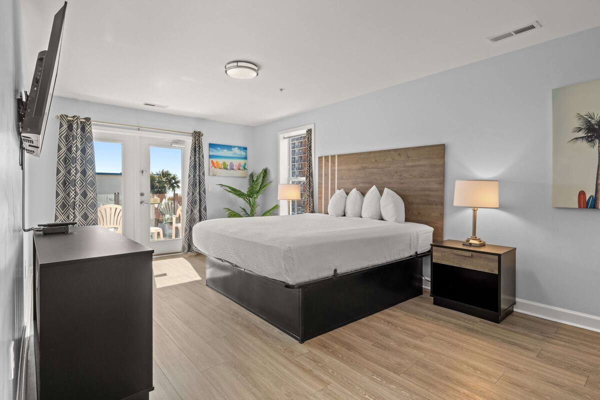 A modern bedroom with a bed, bedside tables, a TV, and a view of the outdoors.