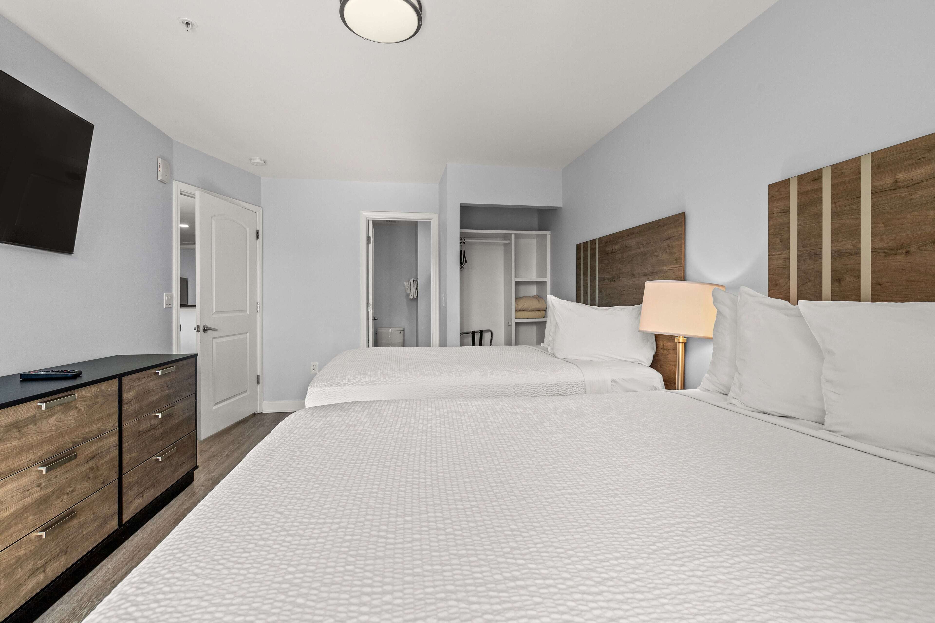 Quarto de hotel moderno com uma cama grande, cômoda de madeira, televisão de tela plana e closet espaçoso.