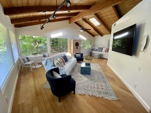 Ein geräumiges Wohnzimmer mit hoher Decke, Holzbalken, einem großen Fernseher und einer gemütlichen Sitzecke mit Sofa und Sesseln.
