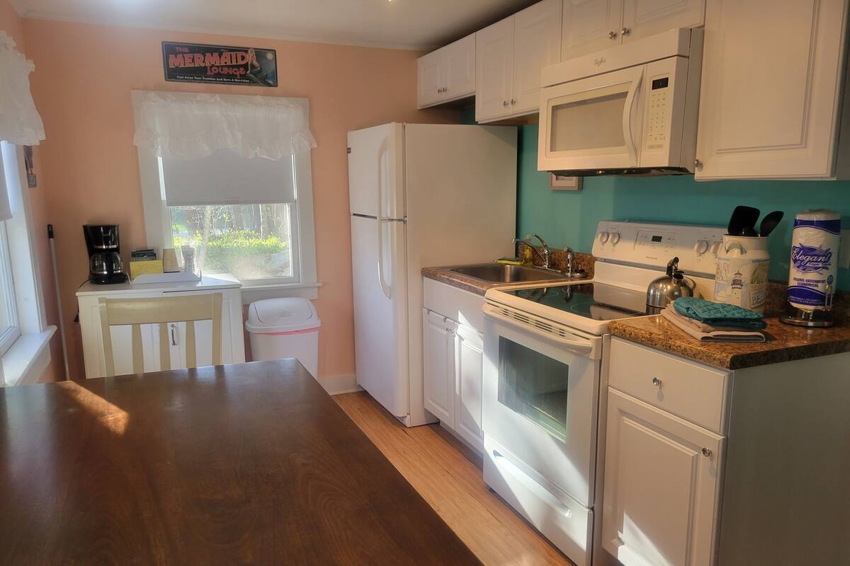 A kitchen with white cabinets, a stove, a sink, and a window with a view of greenery outside.