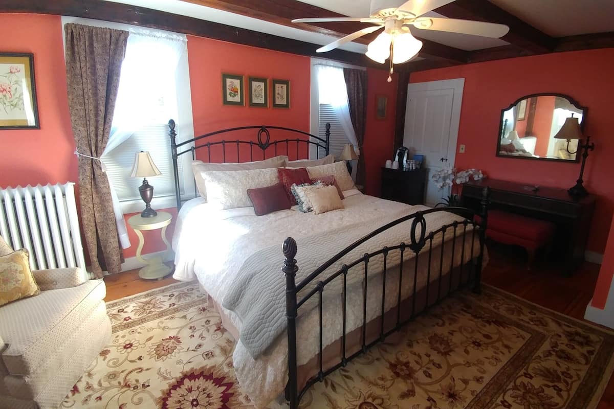 A bedroom with a bed, a chair, a desk, a mirror, and a ceiling fan.