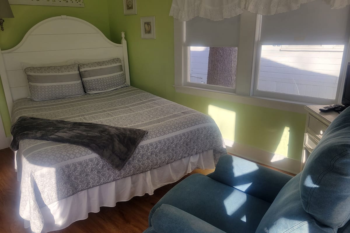 A bedroom with a bed, a chair, a window, and a wall sign.