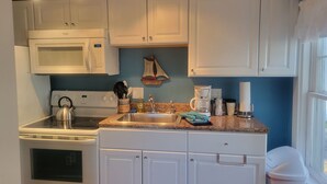 A kitchen with white cabinets, a stove, a microwave, a coffee maker, and a sink. - 2 River Road Inn and Cottages (Cape Neddick)