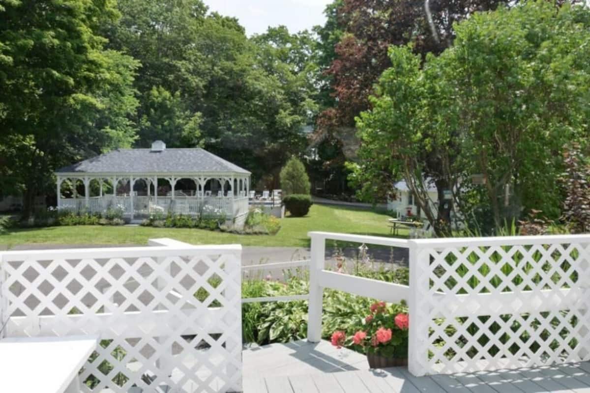 A gazebo in a garden with white lattice fencing and lush greenery.