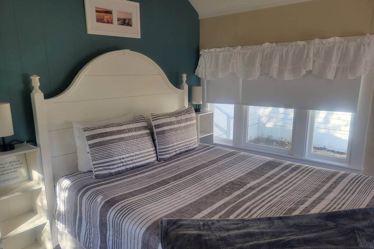 A neatly made bed with striped bedding, a white headboard, and a window with a view of the outside.