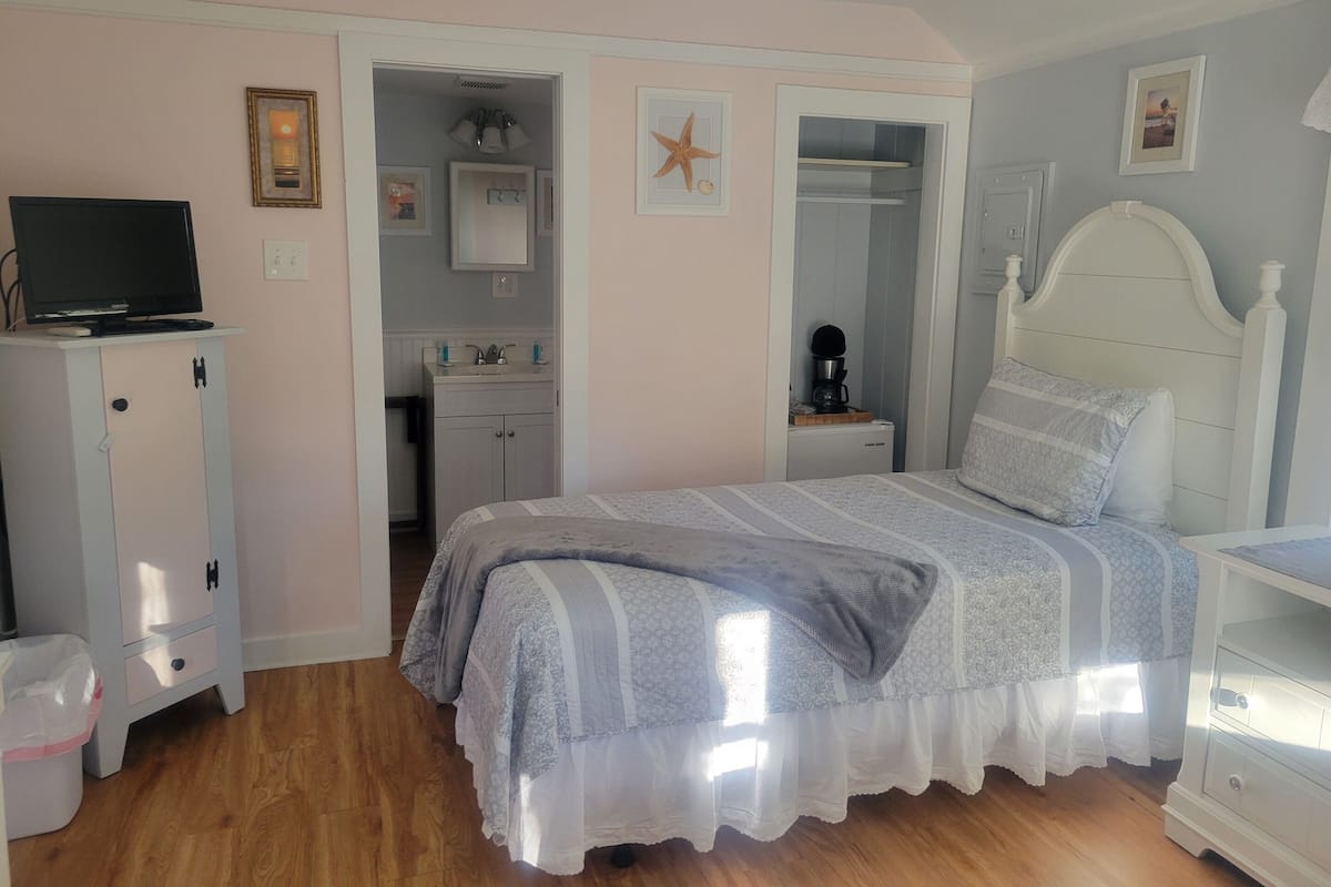 A bedroom with a bed, a nightstand, a dresser, a television on a cabinet, and a bathroom visible through an open door.