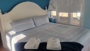 A bedroom with a bed, a nightstand, a window, and a star decoration on the wall. - 2 River Road Inn and Cottages (Cape Neddick)