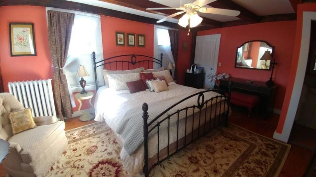 Une chambre à coucher comprenant un lit, une chaise, un radiateur, un ventilateur de plafond et un miroir.