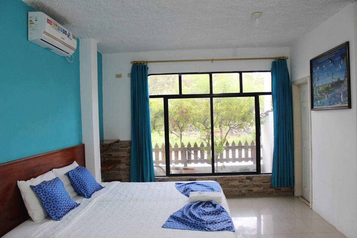 A bedroom with a bed, a window with curtains, a stone wall, and a painting on the wall.