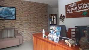 A reception desk with a wooden finish, a framed photograph of a sea turtle, a small turtle figurine, and a sign that reads "Hostal la gran tortuga". - Hotel La Gran Tortuga (Puerto Villamil)