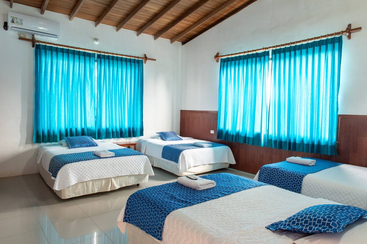 A hotel room with two beds, blue curtains, wooden ceiling beams, and a white air conditioning unit.