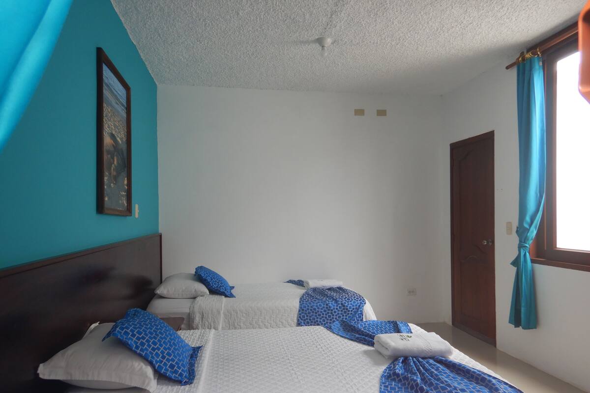 A hotel room with two beds, a ceiling fan, a window with curtains, and a door.