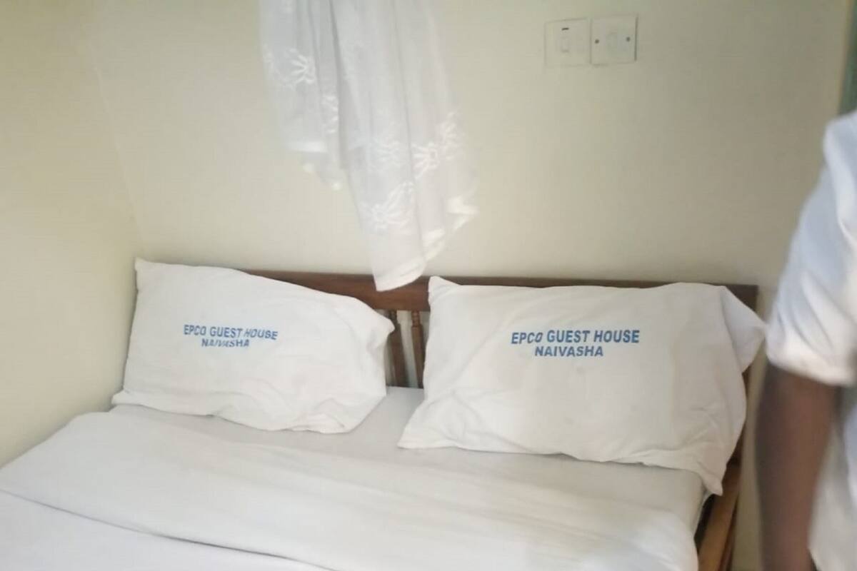 A bed with white bedding and pillows labeled 'EPCO GUEST HOUSE NAIVASHA'.